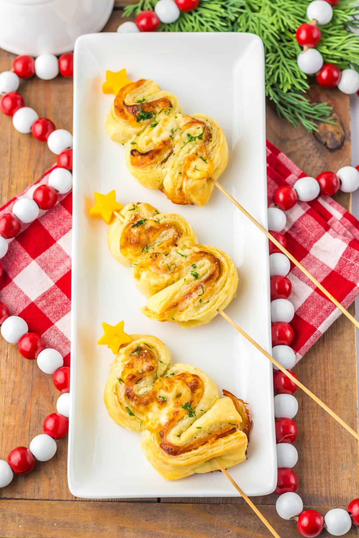 Golden-baked puff pastry Christmas trees with ham and cheese, garnished with parsley and cheddar stars, served on a white platter with holiday decor.