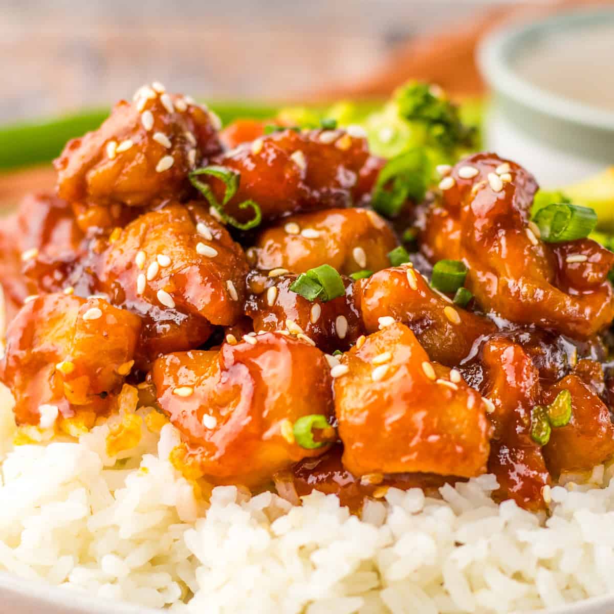 Bourbon chicken like at the mall food court with sesame seeds and green onions over rice, with broccoli in the background.