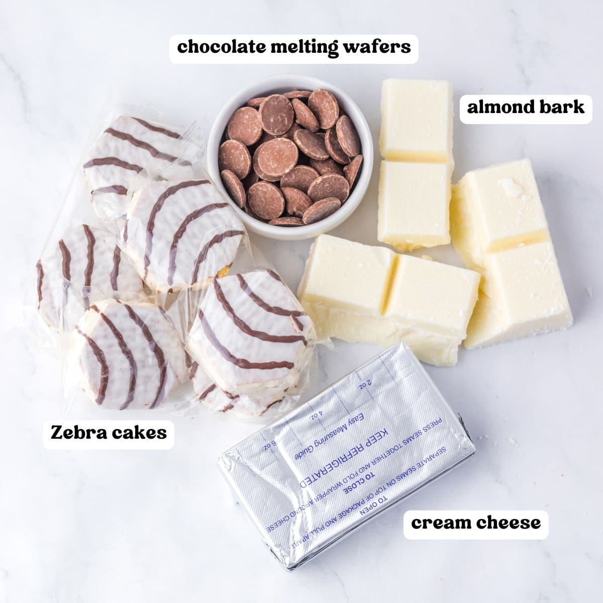 Zebra cakes, chocolate melting wafers, vanilla almond bark, and cream cheese on a white surface, each labeled.