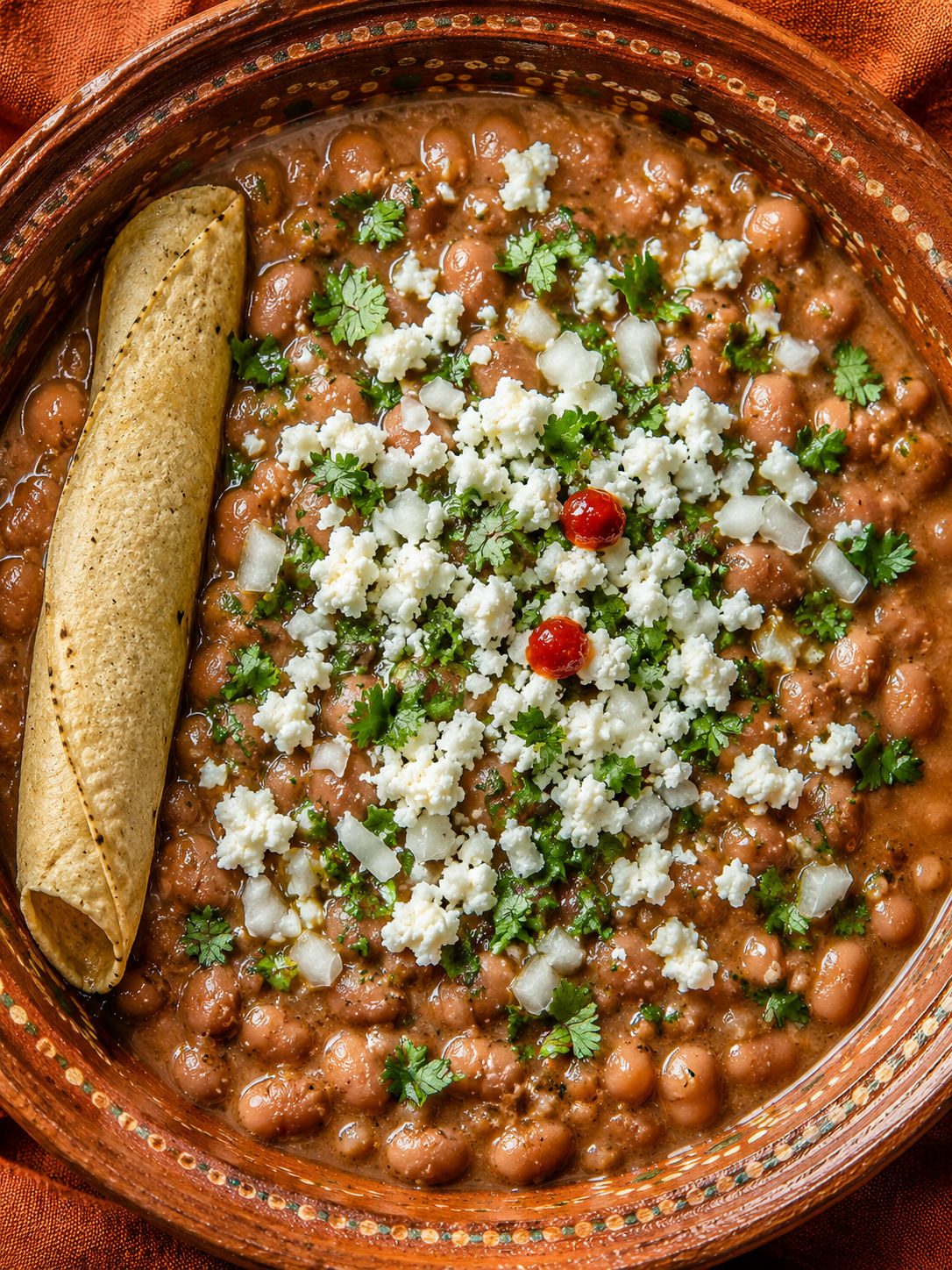 Top-down bowl of creamy frijoles de la olla with queso fresco, cilantro, and lime
